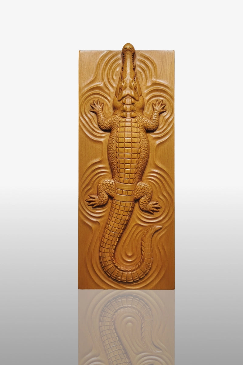 Hand-carved crocodile relief in camphor wood, top-down view with water ripple background