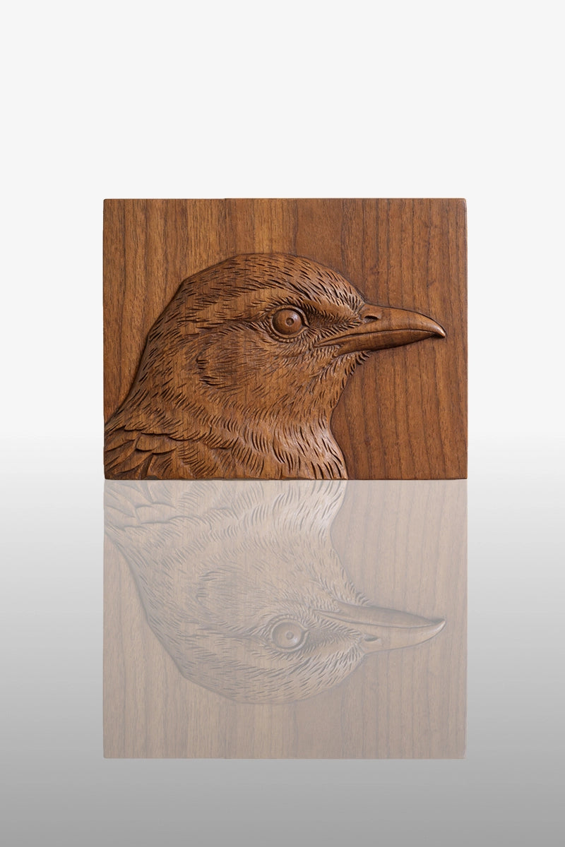 Hand-carved crow head portrait relief in camphor wood with detailed feather texture