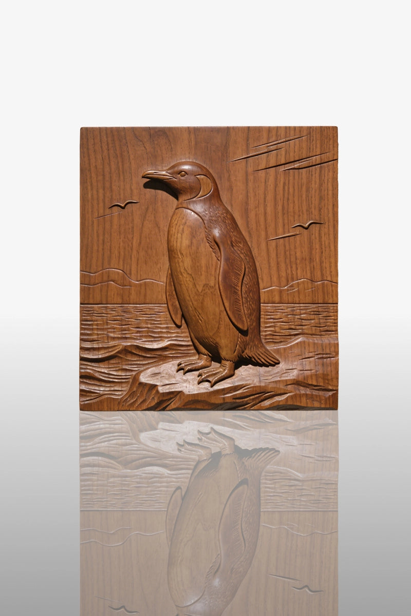 Hand-carved penguin relief in camphor wood standing on rocky shore with ocean background